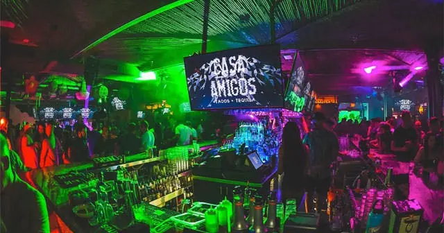 Bar under green and magenta light with screens above the back bar
