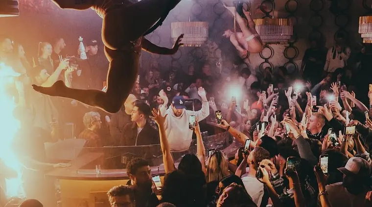 Packed club floor with hands up and phones raised toward a performer