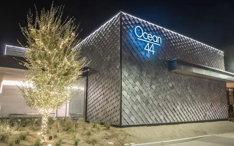 Ocean 44 exterior at night, scaled metal facade and a lit olive tree