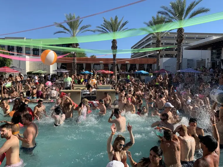 Crowded pool party with streamers, beach balls and swimmers mid-splash