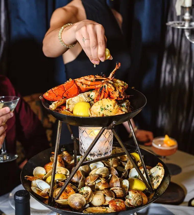 Two-tier seafood tower with lobster, crab and clams being finished with lemon