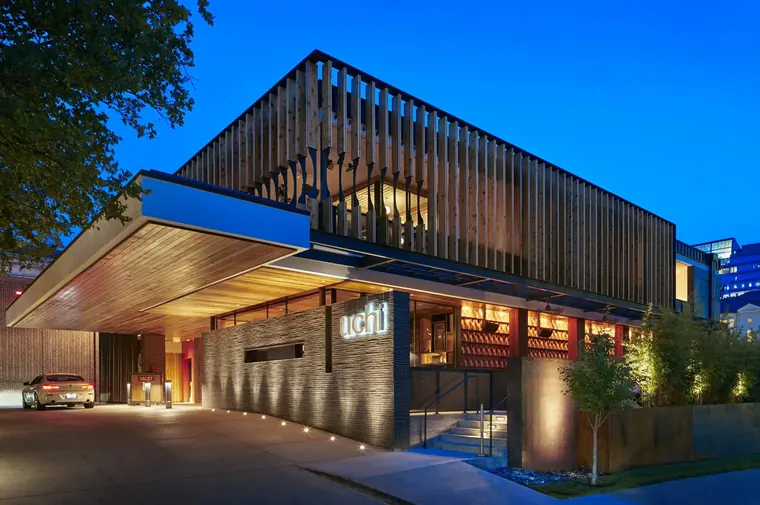 Uchi restaurant exterior lit at blue hour, slatted timber facade over a valet drive